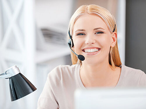 Happy young woman in headset looking at camera and smiling while sitting at her working place